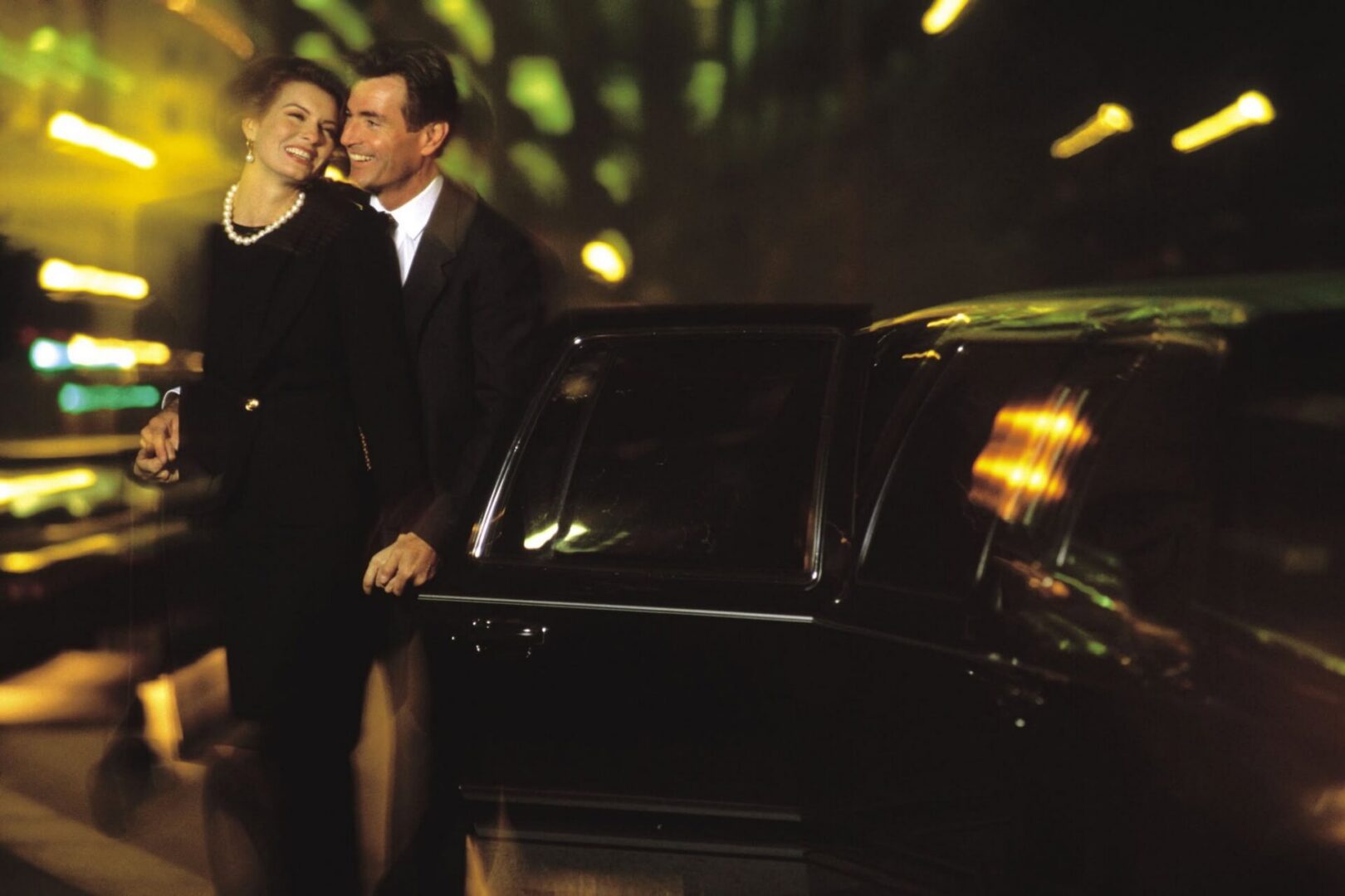 Well-dressed couple laughing beside black car